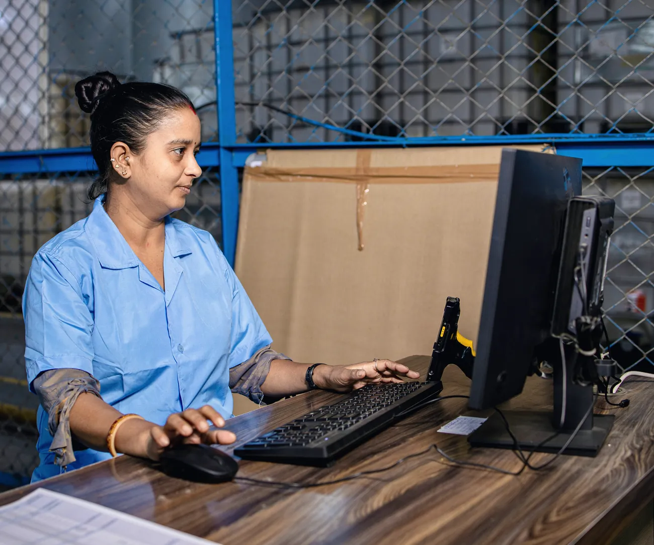 A warehouse worker enters transactions at a desk computer inside a storage cage