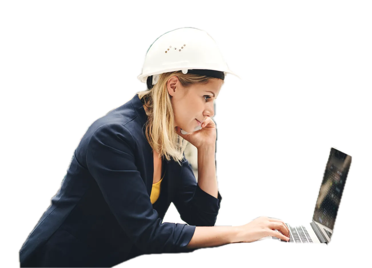 An engineer in a hard hat works on a laptop at a desk in a plant